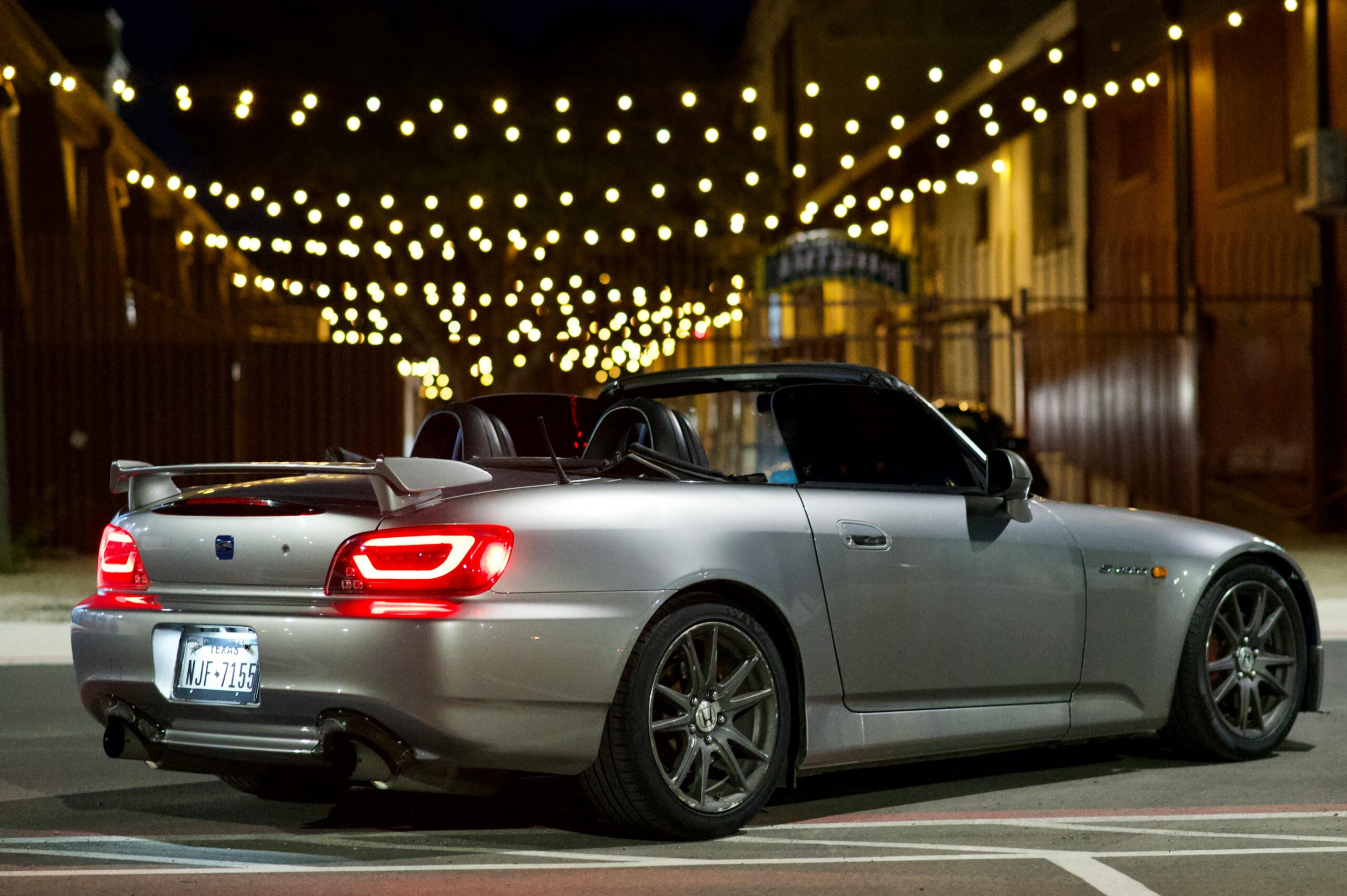 A sleek silver convertible sportscar parked at night beneath elegant string lights, showcasing style and luxury.